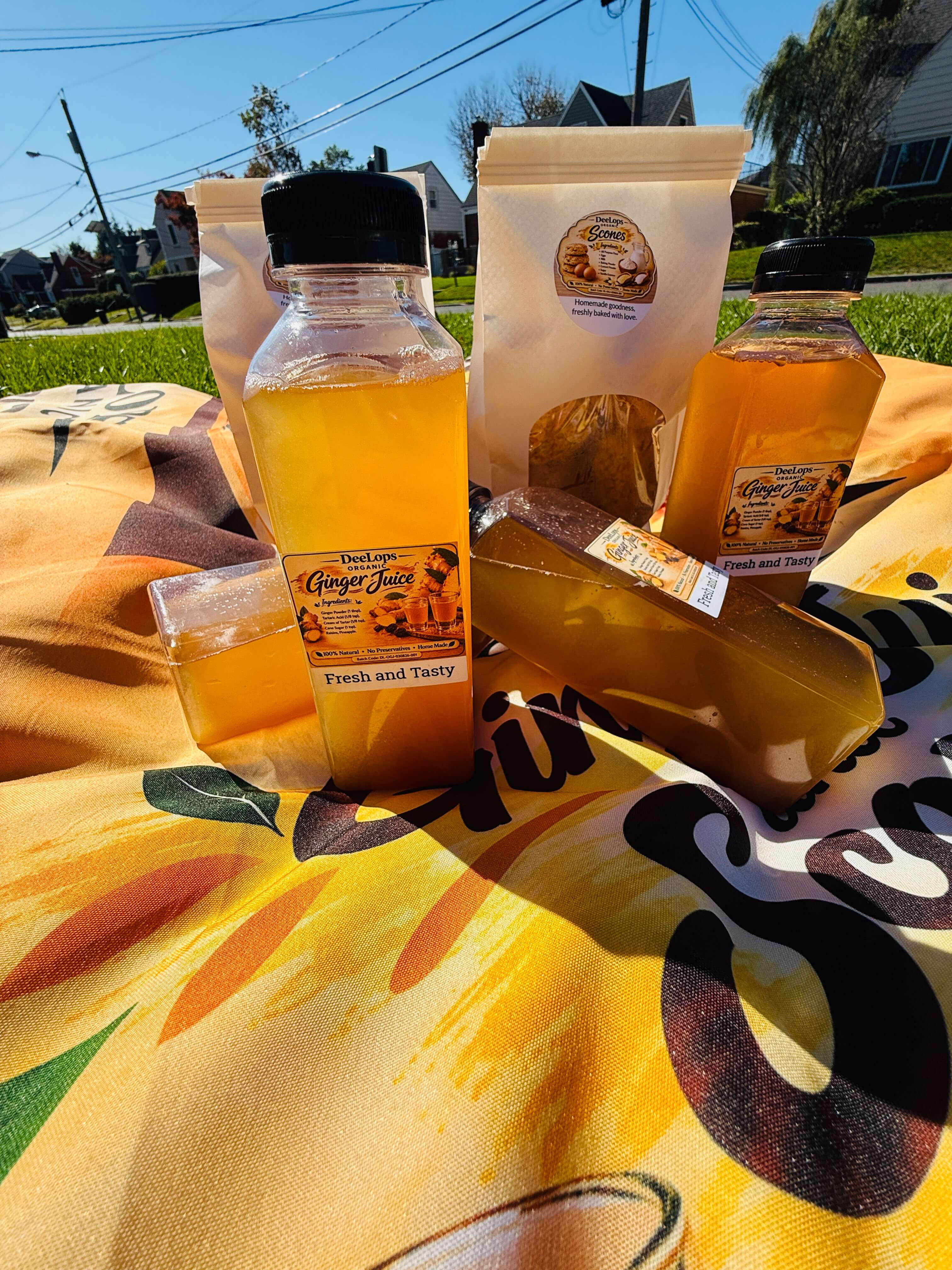 DeeLops Organic Ginger Juice bottles and scone pouches outdoors on a sunny day